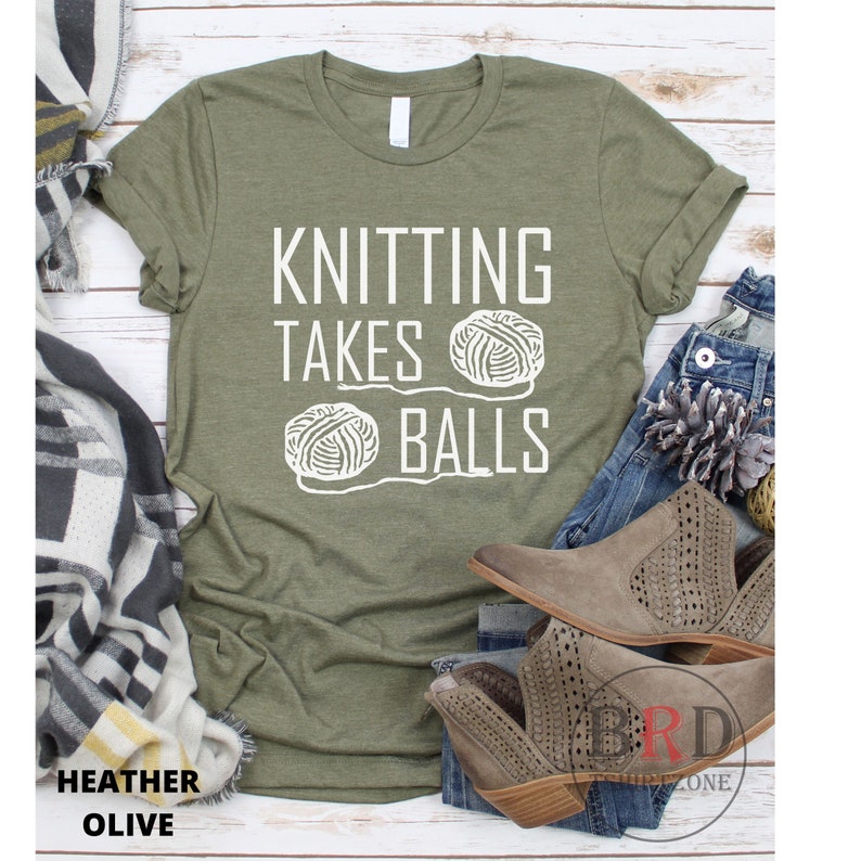 May include: A green t-shirt with the text "Knitting Takes Balls" in white lettering. Two white yarn balls are pictured below the text.