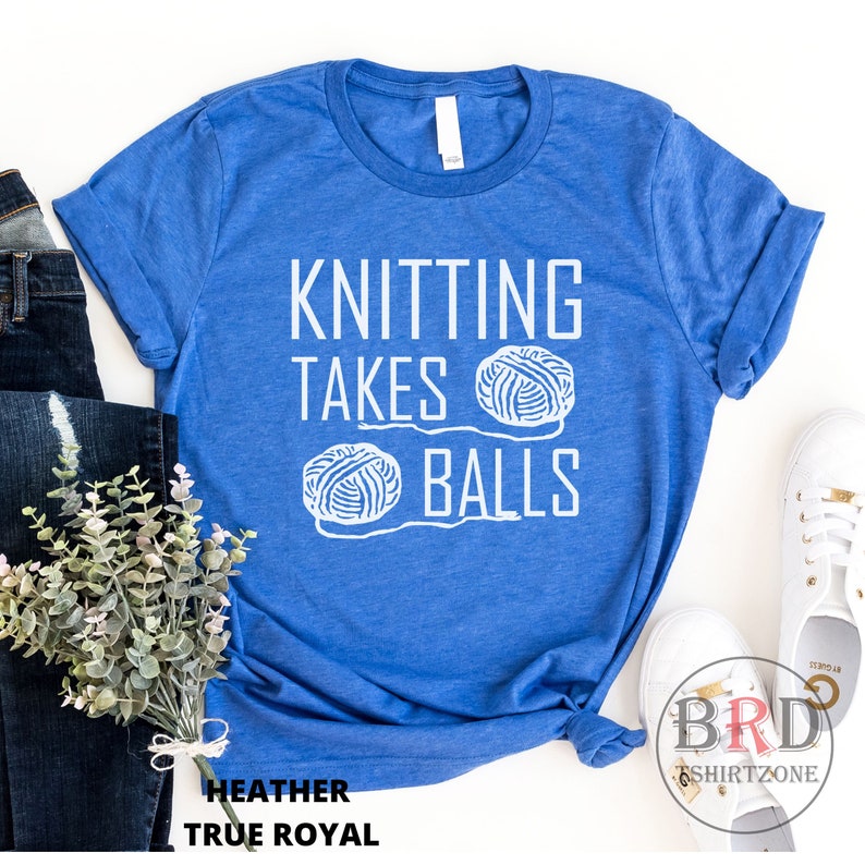 May include: A blue t-shirt with the text "Knitting Takes Balls" in white. Two white yarn balls are pictured next to the text.