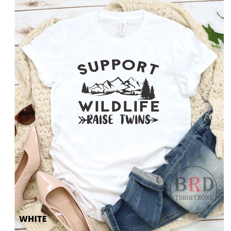 Puede incluir: Camiseta blanca con texto negro que dice "Support Wildlife Raise Twins" con un gr&aacute;fico de monta&ntilde;as y &aacute;rboles.