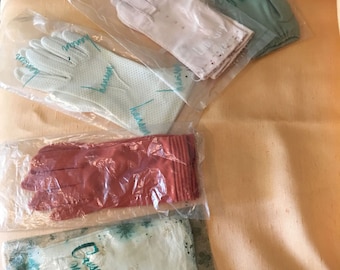 May include: Assortment of vintage gloves in plastic packaging. Includes pairs in light pink, coral, and mint green. One pair has the name "Hansen" printed on it. Another pair has the text "Crescende Wonder Feels".