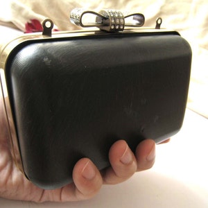 May include: A black leather clutch with a gold metal frame and a rhinestone bow closure.