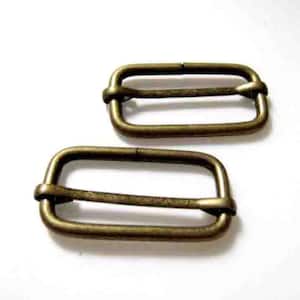 Può includere: Due fibbie scorrevoli in metallo color oro antico. Le fibbie sono rettangolari con angoli arrotondati e hanno un design a doppio anello.