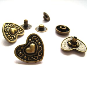 May include: Assortment of antique gold-toned metal heart-shaped buttons with intricate designs. Some buttons have a raised heart in the center.