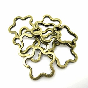 Può includere: Un gruppo di sei portachiavi a forma di stella in metallo color oro antico. I portachiavi sono collegati tra loro e hanno un bordo ondulato e irregolare.