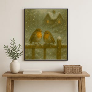 May include: A framed print depicts two robins perched on a wooden fence in a snowy scene. The birds have orange breasts and are facing each other. A house with lit windows is in the background, and snow falls gently. The artwork has a warm, inviting feel.