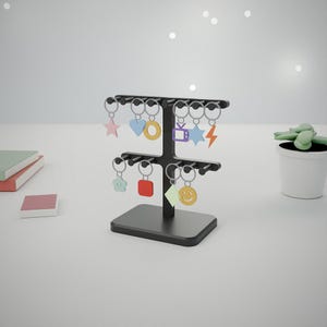 May include: A black two-tiered T-shaped display stand holding multiple keychains with colourful charms in various shapes, including a star, heart, circle, television, lightning bolt, flower, square, diamond, and a smiley face.