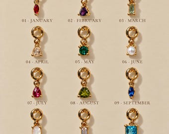 Puede incluir: Doce dijes de metal en tono dorado, cada uno con una piedra preciosa o perla de diferente color. Los dijes están etiquetados del 01 enero al 12 diciembre, mostrando varias formas que incluyen corte de pera, redondo, cuadrado y rectangular.