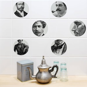 Puede incluir: Una pared de azulejos blancos con retratos en blanco y negro de hombres con bigotes y barbas. Los retratos están dispuestos en una cuadrícula. Una tetera plateada y dos tazas de vidrio están en primer plano.