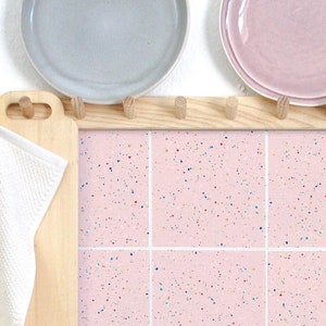 May include: Pink tile with white grout and a speckled pattern of colourful dots. The tile is in a kitchen setting.