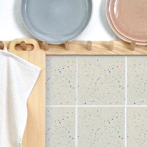 Puede incluir: Nueve azulejos cuadrados con un fondo beige moteado y motas de colores. Los azulejos están dispuestos en una cuadrícula de 3x3.