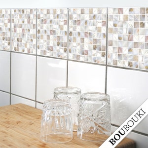 Könnte beinhalten: Eine Küchenszene mit drei klaren, gemusterten Trinkgläsern auf einem Holzschneidebrett. Darüber weiße Fliesen mit einem Mosaikrand aus kleinen, quadratischen Fliesen in Beige, Rosa und Weiß. Das Wort "BOUBOUKI" ist unten rechts sichtbar.