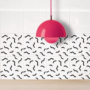 Puede incluir: Una lámpara colgante rosa cuelga sobre azulejos blancos con un patrón geométrico negro. La lámpara tiene una pantalla redonda en forma de cúpula.