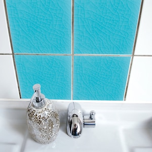 Puede incluir: Un lavabo de porcelana blanca con un grifo cromado y un dispensador de jabón decorativo. El lavabo está delante de una pared con azulejos de patrón azul y blanco.