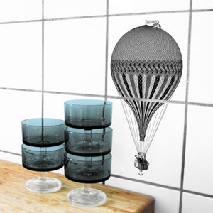 Peut inclure: Quatre coupelles &agrave; dessert en verre transparent empil&eacute;es les unes sur les autres. Les coupelles ont un fond arrondi et un dessus large et plat. Les coupelles sont pos&eacute;es sur une surface en bois. Une illustration en noir et blanc d'une montgolfi&egrave;re avec le texte "Le Voyage" est sur le mur derri&egrave;re les coupelles.