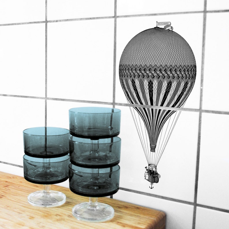 Peut inclure: Quatre coupelles &agrave; dessert en verre transparent empil&eacute;es les unes sur les autres. Les coupelles ont un fond arrondi et un dessus large et plat. Les coupelles sont pos&eacute;es sur une surface en bois. Une illustration en noir et blanc d'une montgolfi&egrave;re avec le texte "Le Voyage" est sur le mur derri&egrave;re les coupelles.
