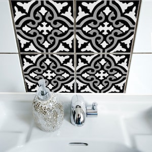 Puede incluir: Cuatro pegatinas de azulejos con patrones en blanco y negro con un diseño geométrico gris y blanco. Las pegatinas se colocan en una pared de azulejos blancos sobre un lavabo de baño blanco con un grifo plateado y un dispensador de jabón de vidrio.