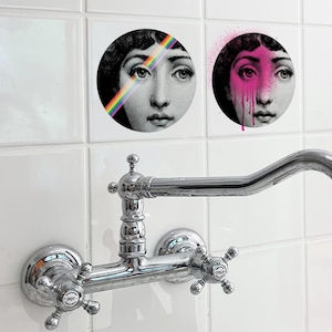 Puede incluir: Dos baldosas decorativas redondas con la cara de una mujer. Una baldosa tiene un arcoíris sobre el ojo, la otra tiene pintura rosa goteando por la cara. Un grifo cromado está montado debajo.