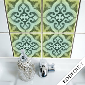Puede incluir: Cuatro pegatinas de azulejos con estampado verde y amarillo con un diseño decorativo. Los azulejos están en una pared de azulejos blancos sobre un lavabo de porcelana blanca con un dispensador de jabón plateado y un grifo plateado.