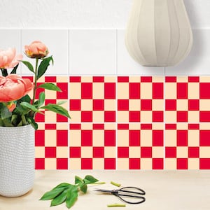 Puede incluir: En esta imagen se muestra un patrón decorativo de cuadros rojos y crema. Un jarrón blanco contiene flores rosas, y unas tijeras y hojas verdes están sobre una superficie de madera. Un jarrón blanco está en el fondo.