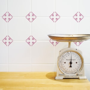 Puede incluir: Balanza de cocina blanca sobre un fondo de azulejos rosa y blanco. La balanza tiene una esfera blanca con números negros y una aguja negra. La balanza indica "Alexanderwerk".