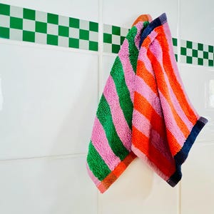 May include: Two striped kitchen towels hanging on a hook. One towel is pink and green, the other is pink and orange.