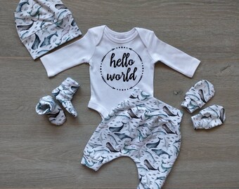 May include: A baby outfit set with a white long-sleeved bodysuit with the text "hello world" in a circle, white pants with a whale and fish pattern, a white hat with a whale and fish pattern, and a pair of white mittens with a whale and fish pattern.