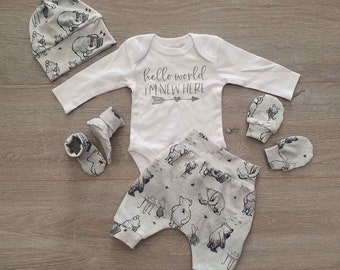 May include: A baby outfit set with a white bodysuit, gray pants, a gray hat, and gray booties. The bodysuit has the text "hello world i'm new here" printed on it. The pants, hat, and booties have a pattern of Winnie the Pooh characters.
