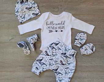 May include: A baby outfit set with a white long-sleeved onesie with the text "hello world i'm new here" and an arrow, white pants with a whale and fish print, a white hat with a whale and fish print, and two pairs of white mittens with a whale and fish print.
