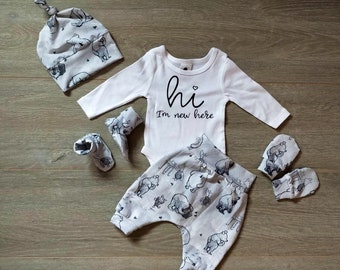 May include: A baby outfit set with a white bodysuit that says "hi I'm new here", grey and white patterned pants, a grey and white hat with a knot on top, and two pairs of grey and white booties.