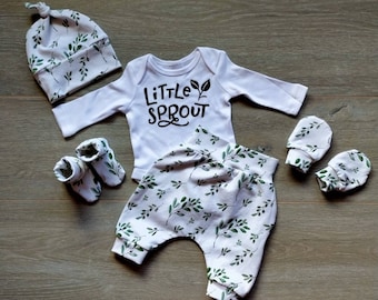 May include: A baby outfit set with a white long-sleeved onesie with the text "Little Sprout", white pants with a green leaf pattern, a white hat with a green leaf pattern, and a pair of white mittens with a green leaf pattern.