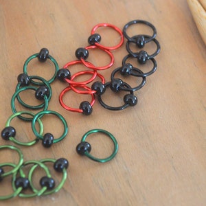 Set of knitting stitch markers on wood background. Rings are lime, green, red and black with black beads.