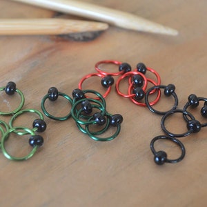 Set of knitting stitch markers on wood background. Rings are lime, green, red and black with black beads.