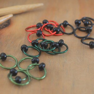 Set of knitting stitch markers on wood background. Rings are lime, green, red and black with black beads.