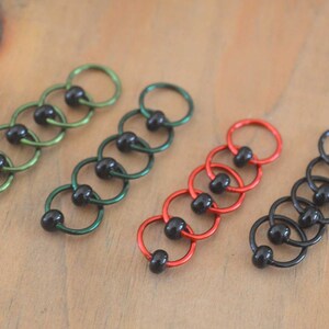 Set of knitting stitch markers on wood background arranged by color. Rings are lime, green, red and black with black beads.