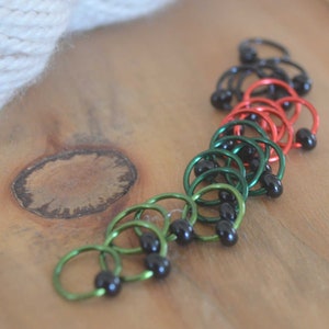 Set of knitting stitch markers on wood background. Rings are lime, green, red and black with black beads.