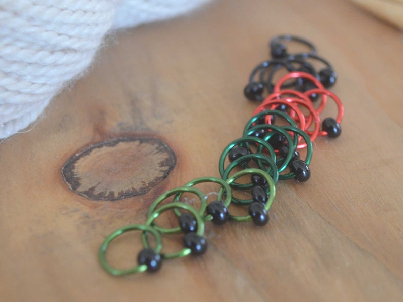 Set of knitting stitch markers on wood background. Rings are lime, green, red and black with black beads.