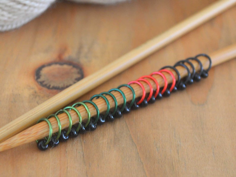 Set of knitting stitch markers on wood background. Rings are lime, green, red and black with black beads.