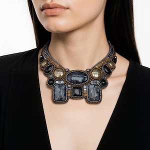 May include: A statement necklace featuring a central oval dark gray stone, flanked by two rectangular gray stones and a smaller black square stone. The piece is embellished with bronze and black beads, along with round translucent stones.