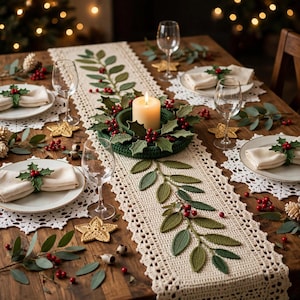 May include: A cream-coloured crocheted table runner featuring green leaf and red berry motifs, centred with a matching crocheted candle ring holding a pillar candle, surrounded by white crocheted placemats and napkins with holly rings.