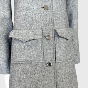 May include: A light gray coat with a textured fabric. The coat features large flap pockets, silver buttons, and a classic collar. The coat's design is simple and elegant, suitable for various occasions.