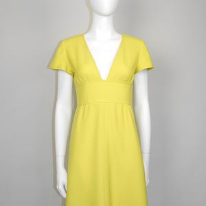 May include: A bright yellow dress with a V-neckline and short sleeves. The dress has a fitted waist and a flowing skirt. The dress is displayed on a mannequin. The dress is a solid color.