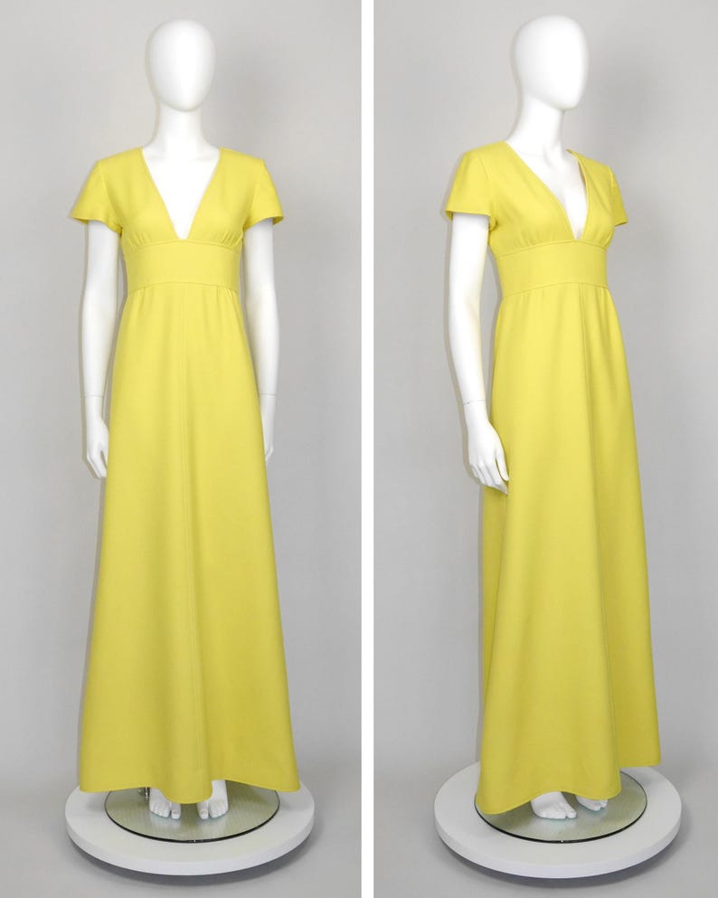 May include: A bright yellow maxi dress with a V-neckline and short sleeves. The dress features a fitted bodice and a flowing skirt. The dress is displayed on a mannequin. The dress is a solid color and appears to be made of a lightweight fabric.