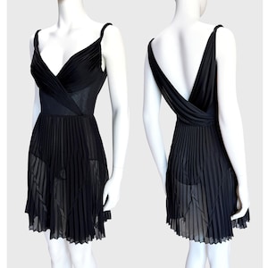 K&ouml;nnte beinhalten: Ein schwarzes Kleid mit einem plissierten Rock und einem V-Ausschnitt-Oberteil. Das Kleid hat d&uuml;nne Tr&auml;ger und einen tiefen R&uuml;cken. Das Oberteil hat ein Wickeldesign, und der Rock ist halbtransparent, wodurch eine flie&szlig;ende Silhouette entsteht. Das Kleid wird auf einer Schaufensterpuppe pr&auml;sentiert.