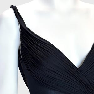 K&ouml;nnte beinhalten: Ein schwarzes Kleid mit drapiertem Oberteil und V-Ausschnitt. Das Kleid hat ein plissiertes Design &uuml;ber der Brust und Tr&auml;ger. Der Stoff scheint ein weiches, flie&szlig;endes Material zu sein.