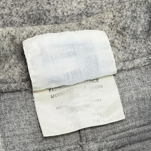 May include: Close-up of gray fabric with a white tag attached. The tag has text that includes "FABRIQUE EN FRANCE" and "MODEL/STYLE 26000". The fabric appears to be a woven material.