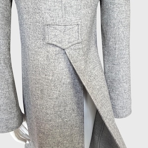 May include: A light gray wool coat with a split back and a small pocket detail. The coat has long sleeves and a tailored fit. The fabric has a subtle texture, and the coat appears to be well-constructed. The coat is displayed on a mannequin.