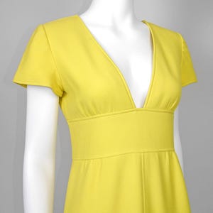 May include: A bright yellow dress with a deep V-neckline and short sleeves. The dress features a fitted waist and a flowing skirt. The fabric appears to be a smooth, solid color, and the dress is displayed on a mannequin.