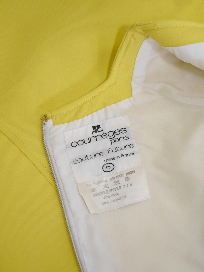 May include: Close-up of a bright yellow garment with a white lining and a zipper. A tag inside the garment reads "courr&egrave;ges paris couture future made in france". The tag also lists fabric content as 100% wool and 100% polyamide.
