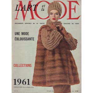 May include: A magazine cover featuring a woman wearing a brown fur coat and a knitted hat. The magazine is titled "L'Art et la Mode" and the text "Documents Officiels de la Haute Couture de Paris" is printed below the title. The magazine cover also features the text "Une Mode Éblouissante" and "Collections 1961".