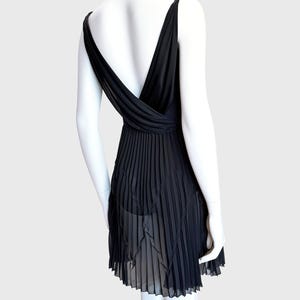 K&ouml;nnte beinhalten: Schwarzes Kleid mit tiefem V-Ausschnitt und plissiertem Rock. Das Kleid hat einen tiefen R&uuml;cken und d&uuml;nne Tr&auml;ger. Der Rock hat ein transparentes, geschichtetes Design. Das Kleid wird auf einer Schaufensterpuppe pr&auml;sentiert.